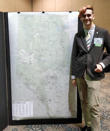 A beaming young man standing next to a wall-height poster.